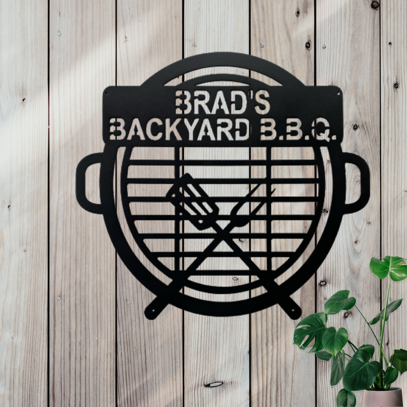 Black metal sign in the shape of a BBQ  grill with 2 grilling tools on it. Near the top there is a place for a personalized name or saying.