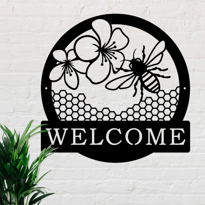 Round metal sign with a bee, flowers and honeycomb in the centre. Banner  at bottom with the word welcome. 