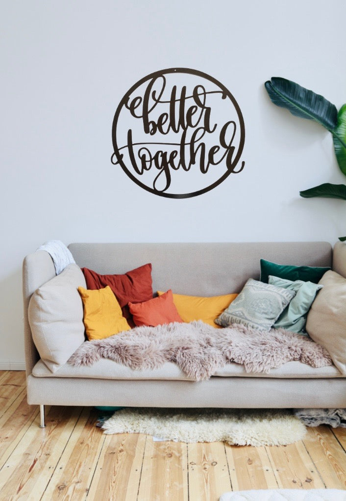 Circular metal sign with the words Better Together hung on a wall above a couch. 