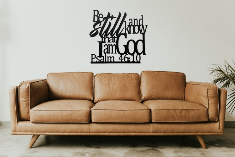 Metal sign showing the Bible verse Psalm 46:10 hanging on wall above couch.