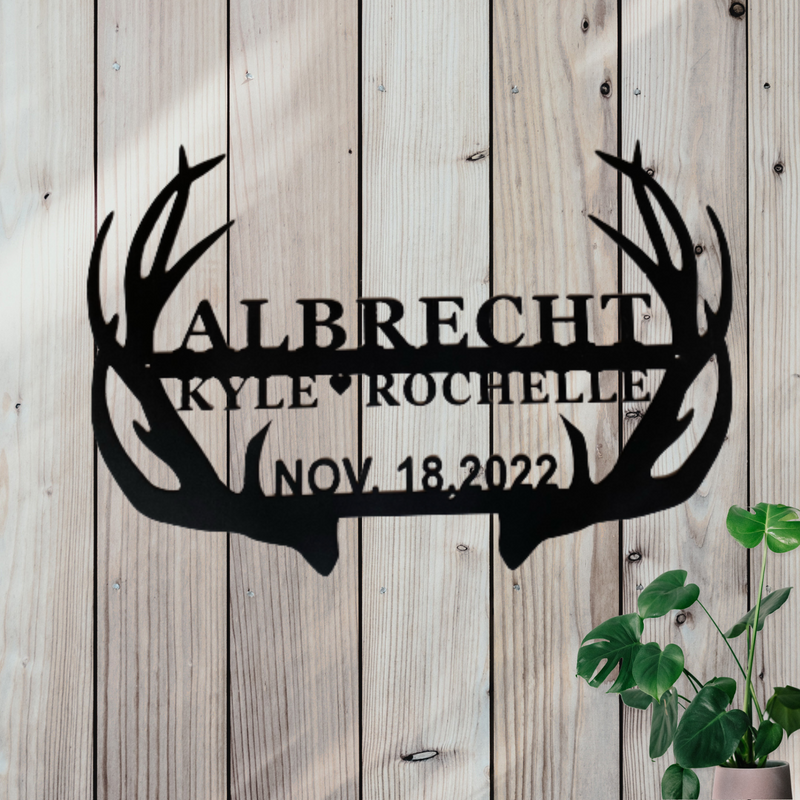 Black metal sign in the shape of antlers with space in the middle for personalized names and date.
