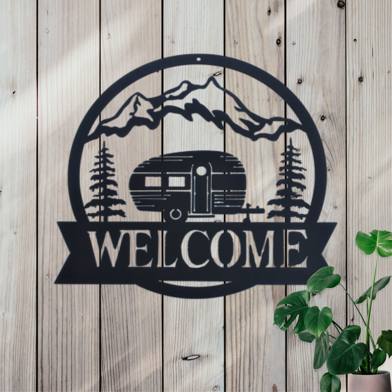 Round Metal sign with a camper, pine trees and mountains and the word Welcome at the bottom. 