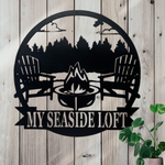 Round black metal sign with 2 muskoka chairs around a bonfire and a row of pine trees behind them. Banner at the bottom of the sign for a custom name.