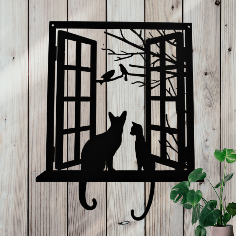 Metal decor showing two cats sitting on a windowsill looking out at birds.