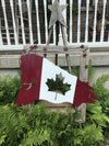 Canadian flag with torn edges displayed in a garden. 
