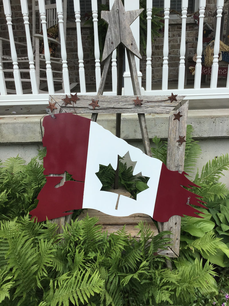 Canadian flag with torn edges displayed in a garden. 